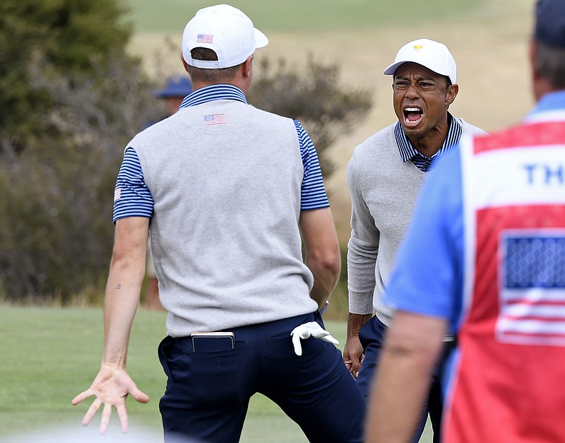 U.S. team member Justin Thomas, left, celebrates with playing partner and captain Tiger Woods on the 18th green after making the winning putt in their foursomes match during the Presidents Cup on Friday at Royal Melbourne Golf Club in Australia. / AP photo by Andy Brownbill