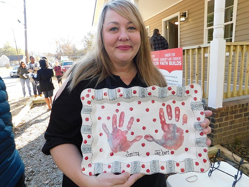 River City Pottery manager Kimberly York holds up a serving platter featuring the handprints of Habitat for Humanity of Greater Chattanooga homeowner Raquel's daughter Somiya and son Jah'Kari. River City invites all local Habitat owners and their families to paint pieces of their choice at the paint-your-own-pottery studio, then presents the finished products to the family at their home's dedication ceremony. / Contributed photo by Habitat for Humanity of Greater Chattanooga