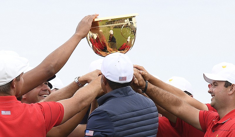 U.S. team members hold up the trophy after winning the Presidents Cup on Sunday at Royal Melbourne Golf Club in Australia. The Americans dominated the singles matches 8-4 to won the overall event 16-14. / AP photo by Andy Brownbill
