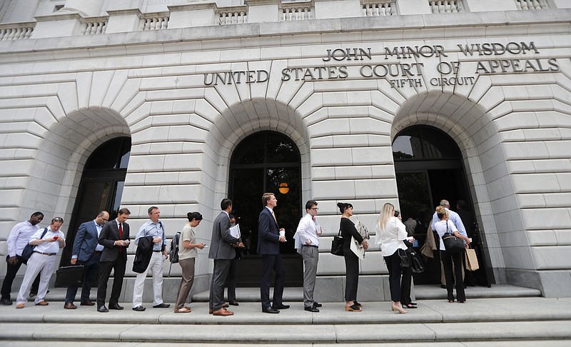 FILE - In this Tuesday, July 9, 2019 file photo, People wait in line to enter the 5th Circuit Court of Appeals to sit in overflow rooms to hear arguments in New Orleans. The “individual mandate" of former President Barack Obama’s health care law is invalid, but other parts of the law need further review, a federal appeals court ruled Wednesday, Dec. 18, 2019. (AP Photo/Gerald Herbert, File)