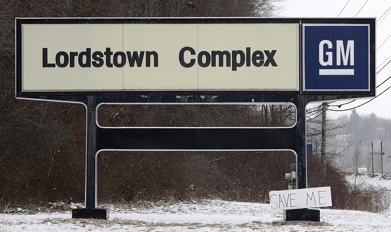 FILE - In this March 6, 2019 file photo, A "Save Me" sign rests against the Lordstown Complex sign in Lordstown, Ohio.  The long-struggling Rust Belt community of Youngstown, Ohio, which was stung by the loss of the massive General Motors Lordstown plant this year, wants to become a research and production hub for electric vehicles.. But Youngstown faces competition from places like Detroit and China that are taking big roles in developing electric vehicles. (AP Photo/Tony Dejak, File)