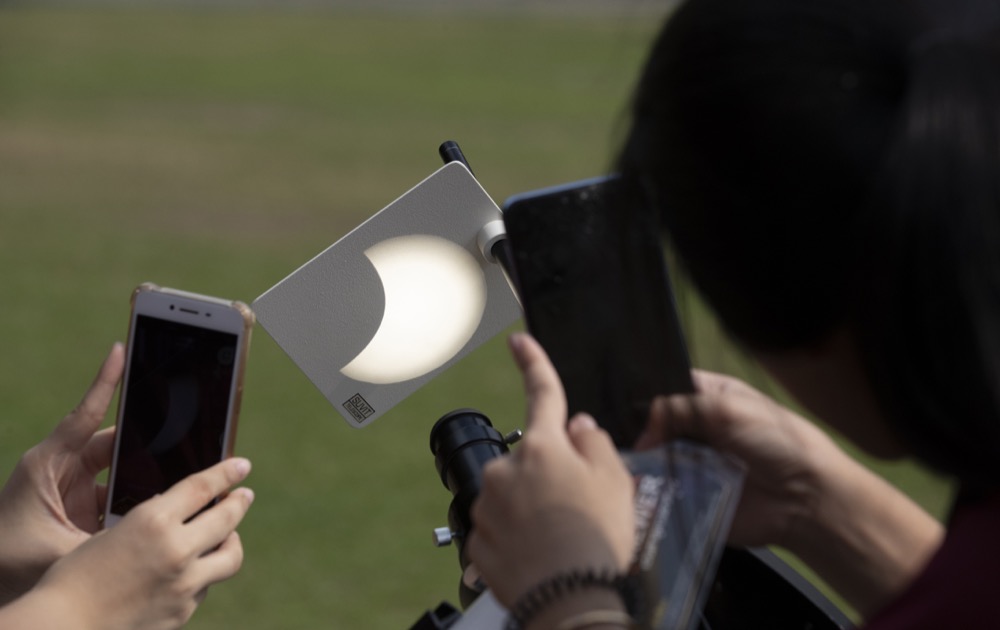 Thai students take a picture by mobile phone observe a partial eclipse as the moon begins to travel a path across the sun at Santiratwitthayalai School in Bangkok, Thailand, Thursday, Dec. 26, 2019. (AP Photo/Sakchai Lalit)