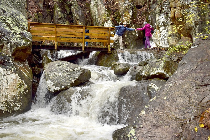 Carl Keiefer helps wife, Stephanie, as they cross over a shallow streams along the Glen Falls Trail on Lookout Mountian on Monday, December 23, 2019.  Stephanie Kiefer is holding the youngest daughter, Cora.  Creeks and streams were on the rise there and across the South. Flash flood watches and warnings covered parts of Tennessee, Georgia, Alabama, Louisiana and South Carolina. / Staff Photo by Robin Rudd  