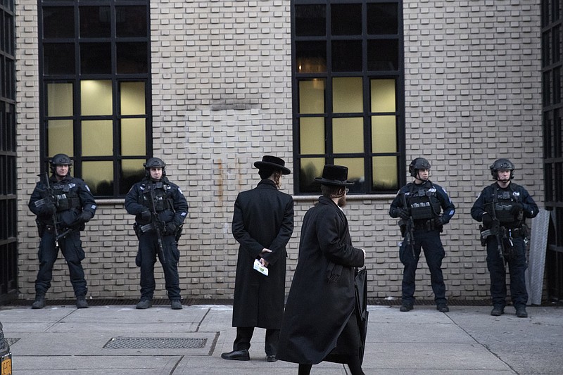 In this Dec. 11, 2019 file photo, Orthodox Jewish men pass New York City police guarding a Brooklyn synagogue prior to a funeral for Mosche Deutsch in New York. Deutsch, a rabbinical student from Brooklyn, was killed in the shooting inside a Jersey City, N.J. market. New York City is increasing its police presence in some Brooklyn neighborhoods with large Jewish populations after a number of possibly anti-Semitic attacks during the Hanukkah holiday. (AP Photo/Mark Lennihan, File)