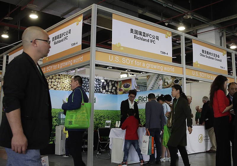 In this April 12, 2018, file photo, visitors walk by U.S. soybean companies' booths at the international soybean exhibition in Shanghai, China. President Donald Trump likes to joke that America's farmers have a nice problem on their hands: They're going to need bigger tractors to keep up with surging Chinese demand for their soybeans and other agricultural goods under a preliminary deal between the world's two largest economies. Yet skeptics are questioning how much China has committed to buy. (AP Photo/Andy Wong, File)