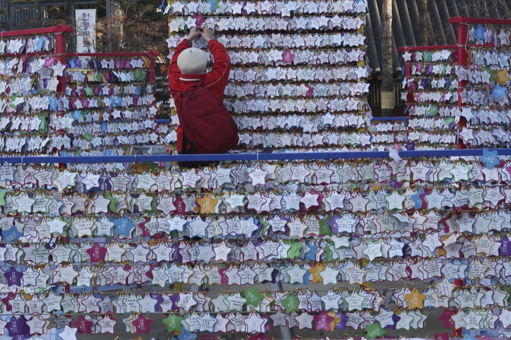 A woman hangs a paper note bearing her New Year wishes to a wire at Jogyesa Buddhist temple in Seoul, South Korea, Tuesday, Dec. 31, 2019. (AP Photo/Ahn Young-joon)