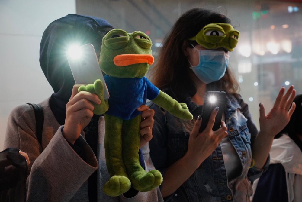 People raise their cellphones lights and stuffed frog toy as they form a human chain on New Year's eve in Hong Kong, Tuesday, Dec. 31, 2019. Months of pro-democracy protests have brought