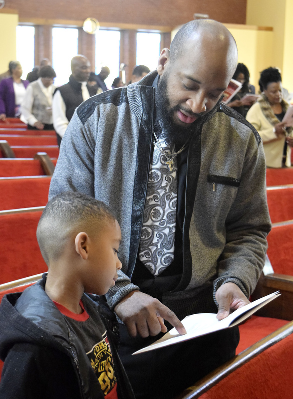 Staff Photo by Robin Rudd/   Darius Lebron Coker helps his son, Darius Lebron Coker Jr., follow the words as they sing the Black National Anthem.