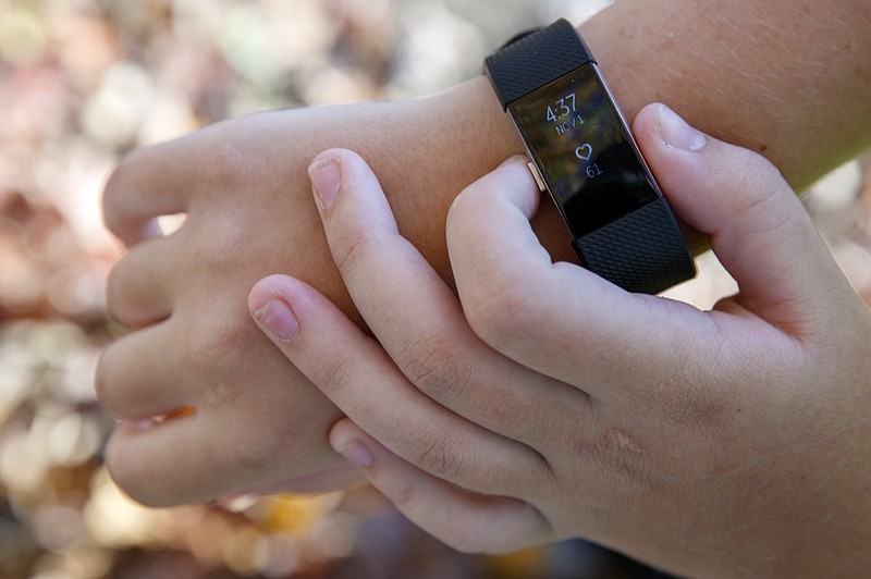 Grace Brown, 14, adjusts her fitness tracker at the park where she does her jogging workouts for her "online PE" class, in Alexandria, Va., Friday, Nov. 1, 2019. Brown chose to take "online PE," utilizing a fitness tracker, so that she could take a piano lab as an extra elective. (AP Photo/Jacquelyn Martin)

