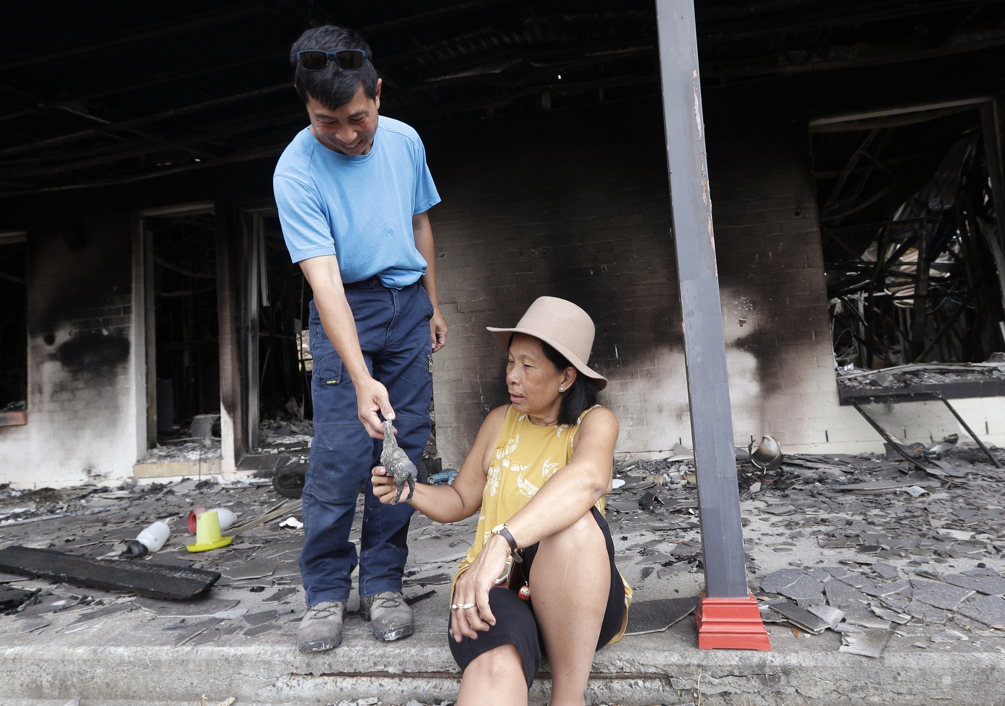 Justin Kam, left, hands to his partner Helena Wong a small horse statue found in the the rubble of their destroyed home at Balmoral, Australia, Tuesday, Jan. 7, 2020. Kam and Wong built their home with quarter-inch thick reinforced glass, steel framing and rock surrounds to protect them from Australia's notorious wildfires. But as they stayed home with their son and battled flames that soared as high as a 15-story building, they realised they were in mortal danger. (AP Photo/Rick Rycroft)