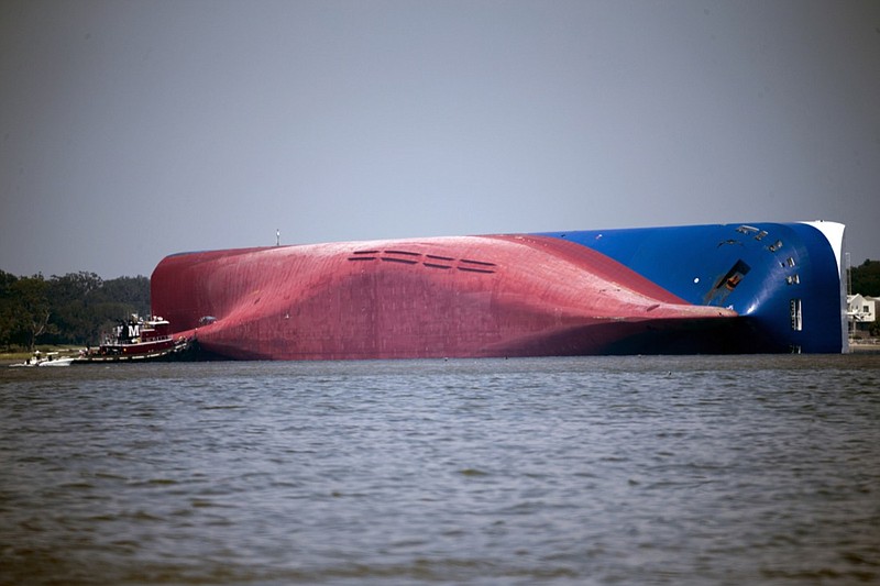 In this Sept. 9, 2019, file photo, a Moran tugboat nears the stern of the capsizing vessel Golden Ray as a tent and rescuers can be seen near the bottom of the ship near the tug boat in Jekyll Island, Ga. A Texas-based salvage company will cut up and remove the 656-foot (200- meter) shipwreck from St. Simons Sound off the coast of Georgia. The Coast Guard's Unified Command has hired T&T Salvage LLC of Galveston to remove the Golden Ray cargo ship, The Brunswick News reported. The ship, roughly the size of a 70-story office building, has sat overturned in the sound for four months. (AP Photo/Stephen B. Morton, File)