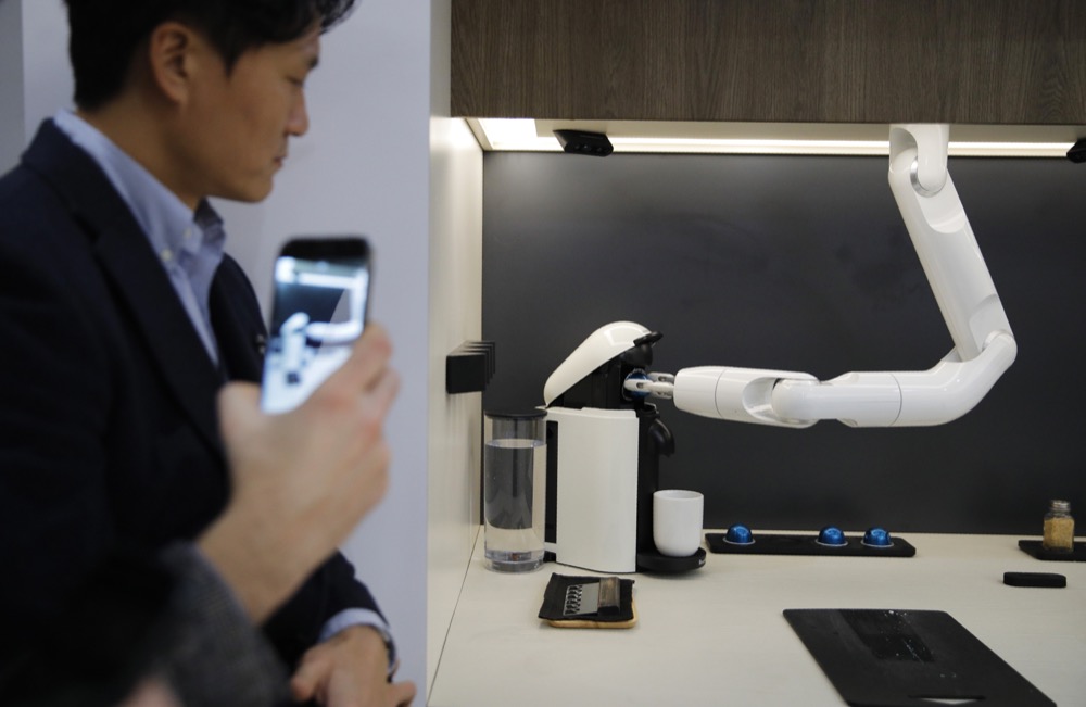 People watch as the Bot Chef makes coffee during a demonstration at the Samsung booth during the CES tech show, Tuesday, Jan. 7, 2020, in Las Vegas. The robot is designed to help with cooking tasks, not to make a meal all on it's own. (AP Photo/John Locher)