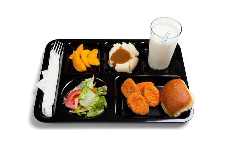 A black school lunch tray including tossed salad, chicken nuggets, roll, peaches, mashed potatoes and gravy with milk on a white background school lunch tile food tile meal tile / Getty Images
