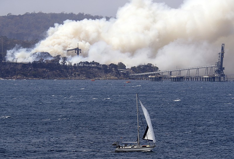 A yacht sails past a burning woodchip mill as the wildfires hits the town of Eden, New South Wales, Australia, Friday, Jan. 10, 2020. The wildfires have destroyed more than 2,000 homes and continue to burn, threatening to flare up again as temperatures rise. (AP Photo/Rick Rycroft)