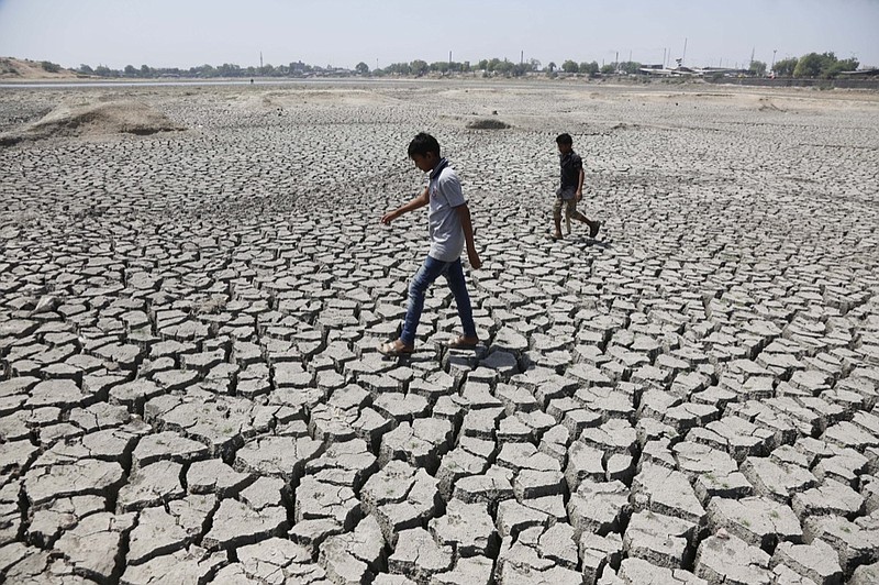 FILE - In this May 14, 2016, file photo, boys on their way to play cricket walk through a dried patch of Chandola Lake in Ahmadabad, India. (AP Photo/Ajit Solanki, File)

