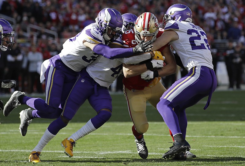 San Francisco 49ers tight end George Kittle, center, is tackled by Minnesota Vikings free safety Harrison Smith, right, and other defenders during the first half of a divisional-round playoff game on Jan. 11 in Santa Clara, Calif. / AP photo by Marcio Jose Sanchez