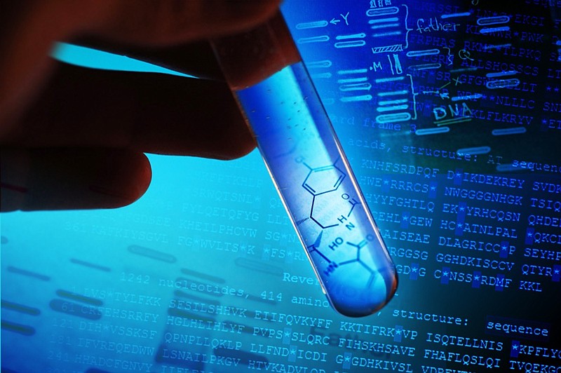 A test tube with blue liquid and a graphic of a partial molecule. There is a hand holding the test tube against a computer image of sequenced DNA. The image is highlighted in dark and light blue. This is a macro image with selective focus. dna tile dna test tile / Getty Images
