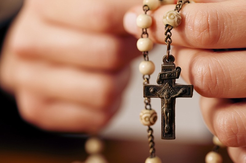 Woman praying with rosary to God - stock photo catholic church tile / Getty Images
