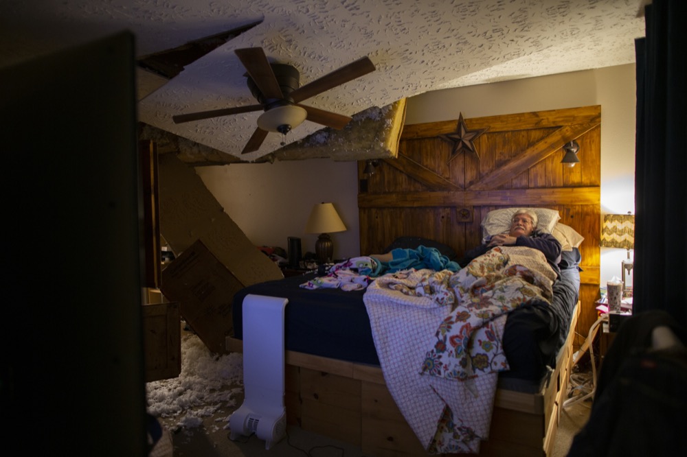 Lee Brewer watches the news from his bedroom as the ceiling hangs after it was damaged by a massive explosion in west Houston on Friday, Jan. 24, 2020, in Houston.  A massive explosion early Friday leveled a warehouse in Houston and damaged nearby buildings and homes, rousing frightened people from their sleep miles away.  (Marie D. De Jesús/Houston Chronicle via AP)