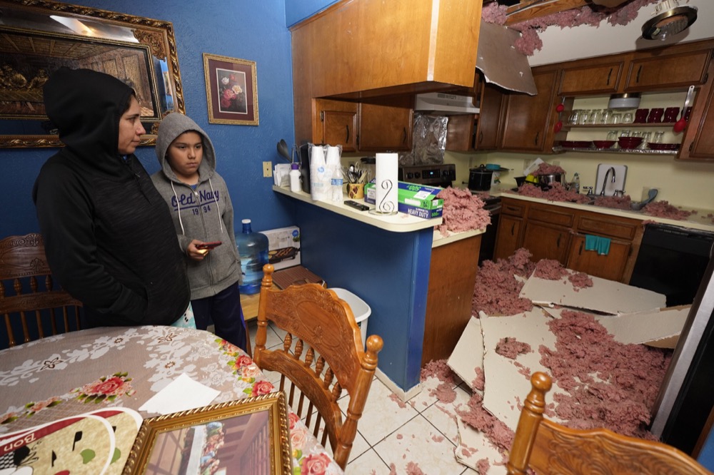 Maria Hernandez and her son, Alejandro Ambriz, 10, stand by the kitchen where the ceiling collapsed in their home, just one street east  where an explosion occurred Friday, Jan. 24, 2020 in Houston.   A massive explosion early Friday leveled a warehouse and damaged nearby buildings and homes, rousing frightened people from their sleep miles away. (Melissa Phillip/Houston Chronicle via AP)