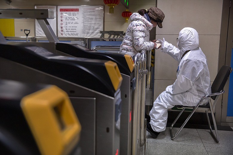 A worker wearing a hazardous materials suit gives directions to a passenger at a subway station in Beijing, Friday, Jan. 24, 2020. China broadened its unprecedented, open-ended lockdowns to encompass around 25 million people Friday to try to contain a deadly new virus that has sickened hundreds, though the measures' potential for success is uncertain. (AP Photo/Mark Schiefelbein)