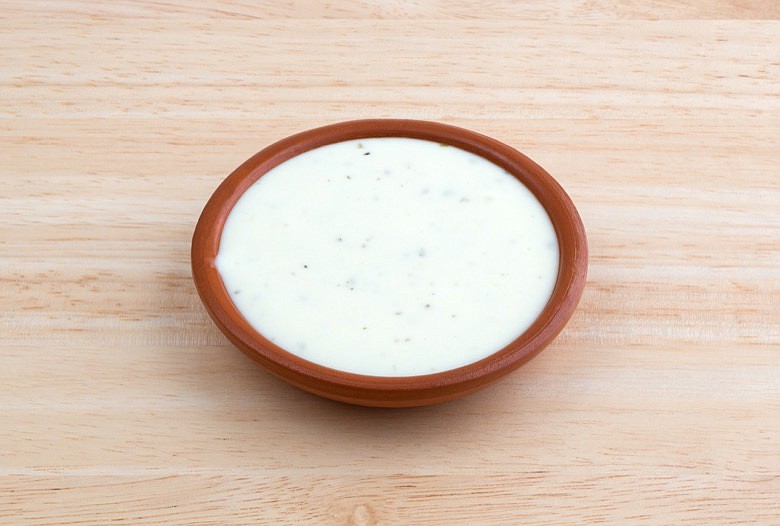 Side view of a small bowl of ranch dressing on a wood table. / Getty Images/iStockphoto/BWFolsom