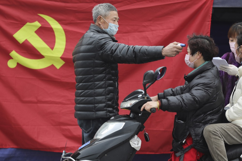 A volunteer stands in front of a Communist Party flag as he takes the temperature of a scooter driver at a roadside checkpoint in Hangzhou in eastern China's Zhejiang Province, Monday, Feb. 3, 2020. China sent medical workers and equipment to a newly built hospital, infused cash into financial markets and further restricted people's movement in sweeping new steps Monday to contain a rapidly spreading virus and its escalating impact. (Chinatopix via AP)