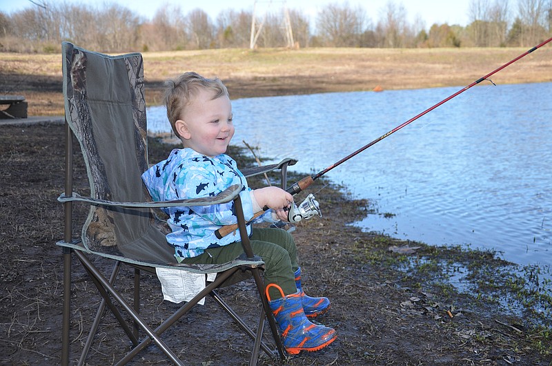 Sunday afternoon at Lake Junior, 2-year-old Asher Gregory sits holding a fishing rod in hopes of catching a trout. He was there with his grandparents, Ted and Christina Gregory. / Photo by Gary Petty
