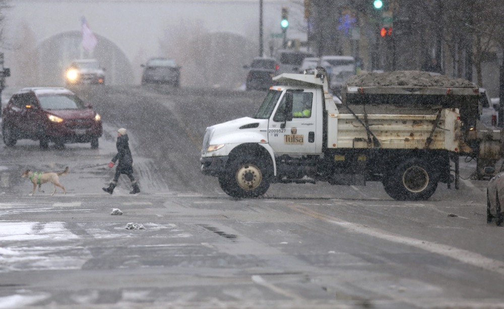 A pedestrian and a sand truck cross Boston Ave. at Sixth street in Tulsa, Okla., on Wednesday, Feb. 5, 2020. A winter storm blanketed the region in snow with forecasters expecting a total of up to 5 inches to fall throughout the Tulsa region. (John Clanton/Tulsa World/Tulsa World via AP)