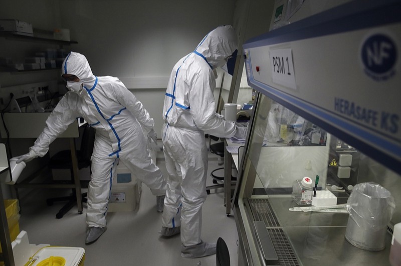 French lab scientists in hazmat gear are seen inserting liquid in test tube manipulate potentially infected patient samples at Pasteur Institute in Paris, Thursday, Feb. 6, 2020. Scientists at the Pasteur Institute developed and shared a quick test for the new virus that is spreading worldwide, and are using genetic information about the coronavirus to develop a potential vaccine and treatments. (AP Photo/Francois Mori)

