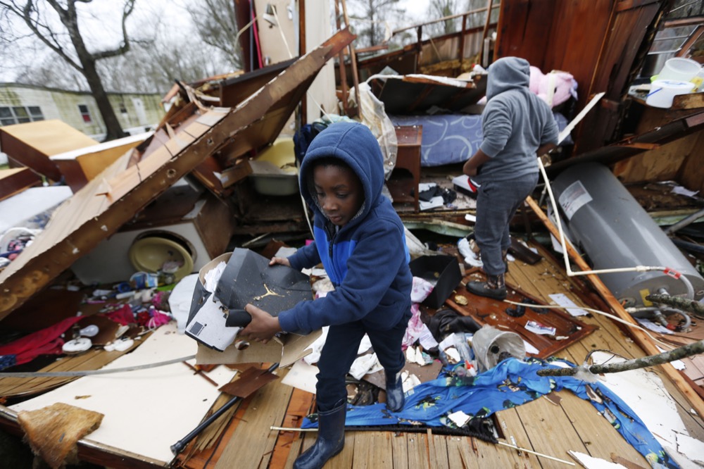 Emma Carter's grandsons comb the remains of her mobile home in Pickens, Miss., looking for salvageable clothing and personal items after severe weather hit the area, Thursday, Feb. 6, 2020. None of the other mobile homes adjacent to the Carter's were destroyed when the winter storm hit Wednesday. (AP Photo/Rogelio V. Solis)