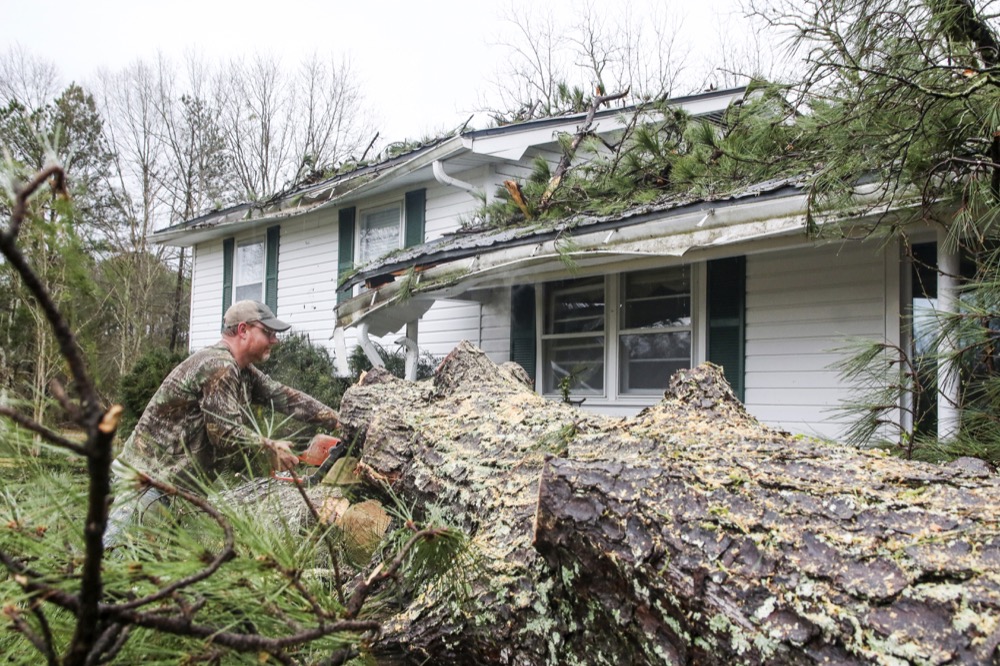 Austin Cochran uses a chainsaw to cut away a large tree that fell on the home of Gerald Covington on Old Mill Creek Road in Enterprise, Miss. Severe storms pounded the area throughout Wednesday, Feb. 5, 2020, and Thursday morning. (Paula Merritt/The Meridian Star via AP)