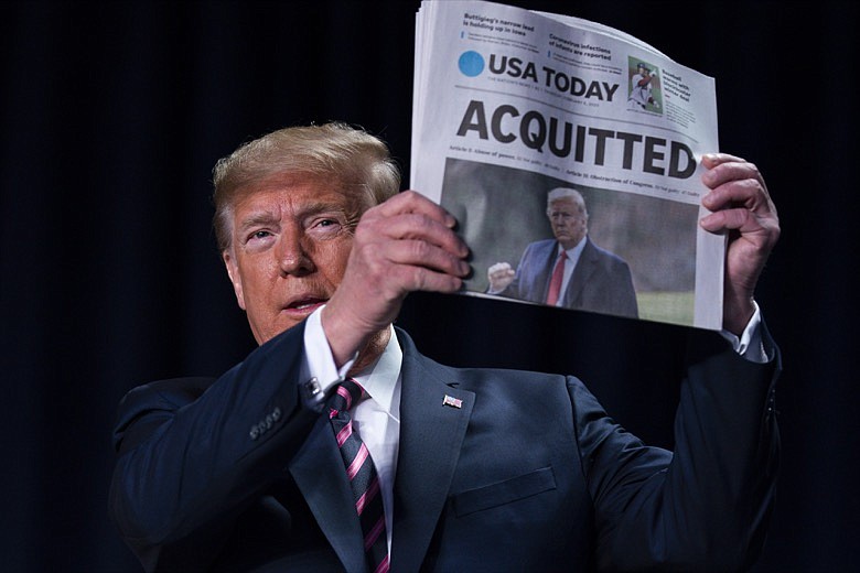President Donald Trump holds up a newspaper with the headline that reads "ACQUITTED" at the 68th annual National Prayer Breakfast, at the Washington Hilton, Thursday, Feb. 6, 2020, in Washington. (AP Photo/ Evan Vucci)