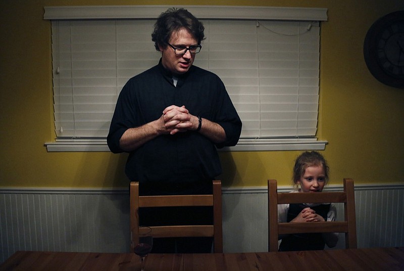 In this Feb. 7, 2020, photo, converted Catholic Priest Joshua Whitfield, left, his daughter Zoe-Catherine, 5, and the rest of his family stand behind their chairs to say grace before dinner in north Dallas. (AP Photo/Jessie Wardarski)

