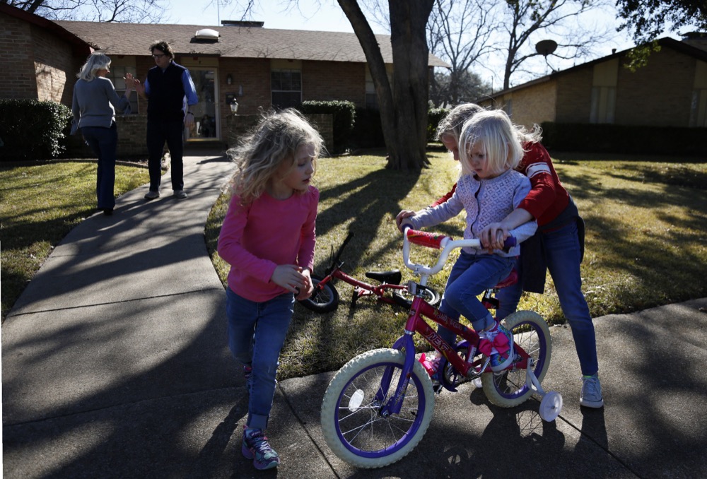 In this Feb. 8, 2020, photo, Alli Whitfield, left, high-fives husband and Catholic Priest Joshua, as their three daughters Zoe-Catherine, 5, Bernadette, 4, and Maggie, 9, ride bikes outside of their home in north Dallas. (AP Photo/Jessie Wardarski)