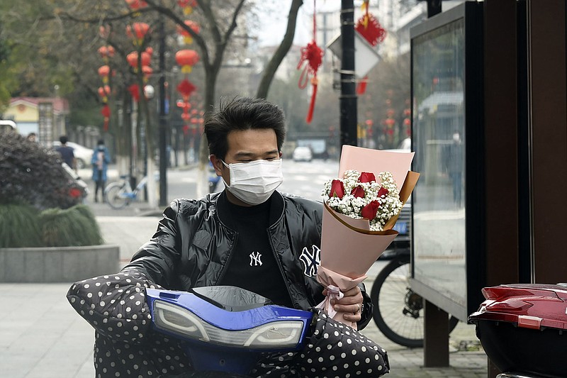 A man wearing a face mask carries a Valentine's Day bouquet as he rides a scooter in Hangzhou in eastern China's Zhejiang Province, Friday, Feb. 14, 2020. China on Friday reported another sharp rise in the number of people infected with a new virus, as the death toll neared 1,400. (Chinatopix via AP)

