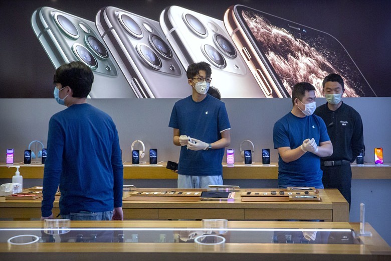 In a Feb. 14, 2020 file photo, employees wear face masks as they stand in a reopened Apple Store in Beijing. Apple Inc. is warning investors that it won't meet its second-quarter financial guidance because the viral outbreak in China has cut production of iPhones. The Cupertino, California-based company said Monday, Feb. 17, 2020 that all of its iPhone manufacturing facilities are outside Hubei province, and all have been reopened, but production is ramping up slowly. (AP Photo/Mark Schiefelbein, File)