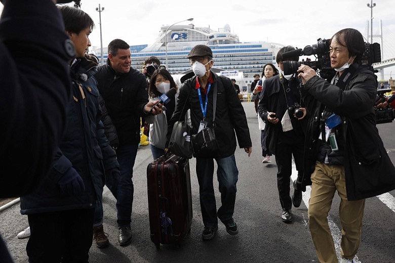 An unidentified passenger is surrounded by the media after he disembarked from the quarantined Diamond Princess cruise ship Wednesday, Feb. 19, 2020, in Yokohama, near Tokyo. Passengers tested negative for COVID-19 started disembarking Wednesday. (AP Photo/Jae C. Hong)