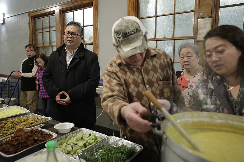 In this Sunday, Feb. 16, 2020, photo Baptist Pastor Clifford Maung, third from left, recites a prayer as Chin Sai, center, and Myint Myint Swe, right, prepare food following services at the Overseas Burmese Christian Fellowship in Boston. All three are immigrants from Myanmar, also known as Burma. Confusion, sorrow and outrage are rippling across some immigrant communities after the announcement of a Trump administration policy that is expected to all but shut down family-based immigration from four countries, including Myanmar. (AP Photo/Steven Senne)