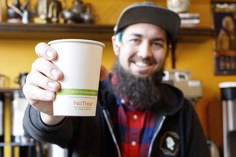 Staff photo by C.B. Schmelter / Michael Rice shows off a compostable coffee cup at The Mad Priest Coffee & Cocktails.