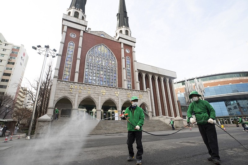 Workers wearing face masks spray disinfectant as a precaution against the new coronavirus in front of Myungsung Church in Seoul, South Korea, Wednesday, Feb. 26, 2020. The number of new virus infections in South Korea jumped again Wednesday and the U.S. military reported its first case among its soldiers based in the Asian country, with his case and many others connected to a southeastern city with an illness cluster. (Yun Dong-jin/Yonhap via AP)