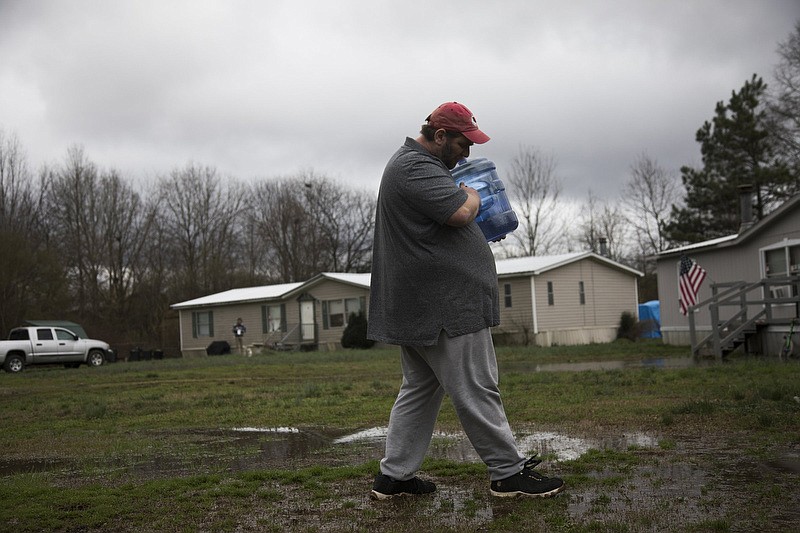 Staff photo by Troy Stolt / Carey Laughlin carries a water container from into his daughter's house on Thursday, Feb. 13, 2020 in Summerville, Georgia.  On January 31st, Summerville residents were advised not to consume their tap water after cancer causing chemicals were discovered during a quality inspection done by the Environmental Protection District of Georgia. Laughlin, who lives with his wife, his 70 year old mother, and three dogs, also has a heart condition that forces him to take medication that he must drink a lot of water with, though water is available at Summerville City Hall, their supply is shrinking steadily, leaving Laughlin to wonder how this situation will be fixed. 