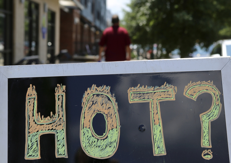 Staff photo by C.B. Schmelter / A pedestrian walks his dog past a sign, advertising cold drinks by asking costumers if they are hot, in front of Walnut Bridge Market on Wednesday, July 19, in Chattanooga, Tenn.