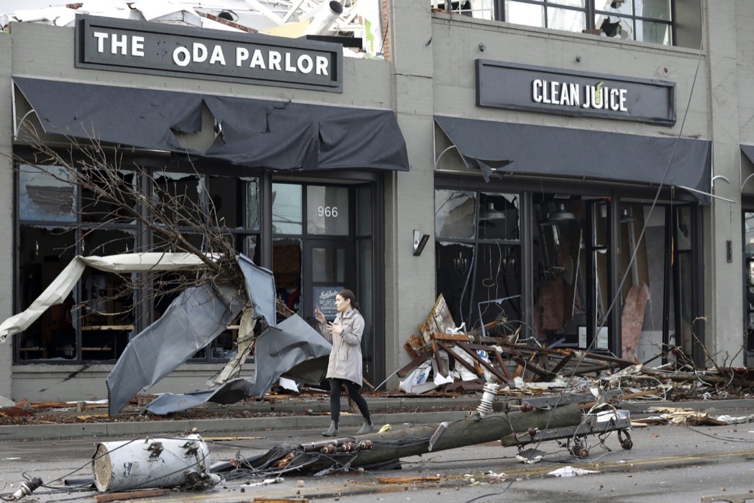 A woman walks past buildings damaged by storms Tuesday, March 3, 2020, in Nashville, Tenn. At least two tornadoes touched down early Tuesday in central Tennessee, including one that ripped across areas near downtown Nashville and caused multiple buildings to collapse. (AP Photo/Mark Humphrey)