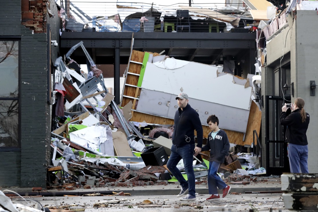 People walk past buildings damaged by storms Tuesday, March 3, 2020, in Nashville, Tenn. At least two tornadoes touched down early Tuesday in central Tennessee, including one that ripped across areas near downtown Nashville and caused multiple buildings to collapse. (AP Photo/Mark Humphrey)
