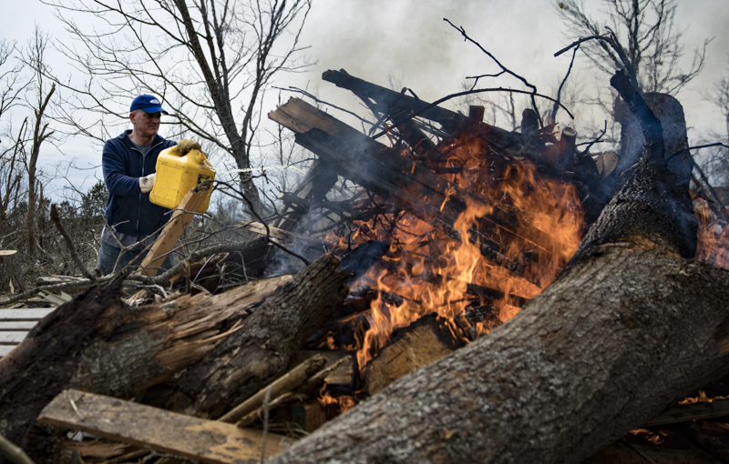 Staff photo by Troy Stolt / Brad Downs, a volunteer who came to help Cookeville residents who lost their homes in the tornado on Tuesday, throws Diesel onto a debris fire in Cookeville, Tenn. on Wednesday, March 4, 2020. A tornado destroyed 140 buildings in Putnam County early Tuesday, killing at least 18 people, and leaving many without homes.