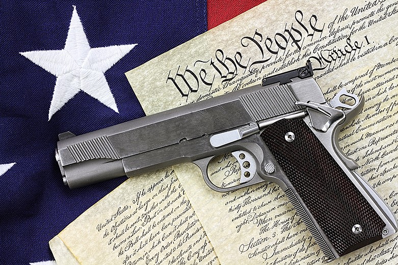 Handgun lying over a copy of the United States constitution and the American flag. / Getty Images/iStockphoto/StephanieFrey