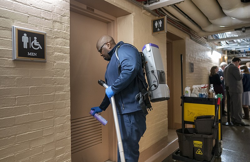 Photo by J. Scott Applewhite of The Associated Press / A worker with the the Architect of the Capitol staff sprays a disinfectant on a restroom door to sanitize the area as House Democrats meet nearby on a coronavirus aid package on Capitol Hill Wednesday, March 11, 2020.