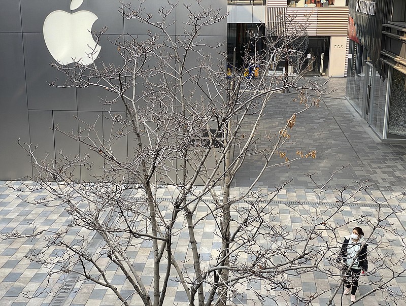 A woman wearing mask walks past the Apple store in an empty mall district in Beijing, China on Wednesday, Feb. 26, 2020. The tech giant Apple has reopened some of its stores in China but says the viral outbreak is starting to disrupt its supplies. (AP Photo/Ng Han Guan)


