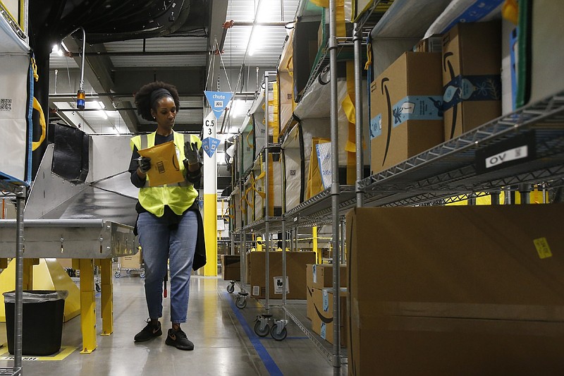FILE - In this Dec. 17, 2019, file photo, Tahsha Sydnor stows packages into special containers after Amazon robots deliver separated packages by zip code at an Amazon warehouse facility in Goodyear, Ariz. On Monday, March 16, 2020, Amazon said that it needs to hire 100,000 people across the U.S. to keep up with a crush of orders as the coronavirus spreads and keeps more people at home, shopping online. (AP Photo/Ross D. Franklin, File)
